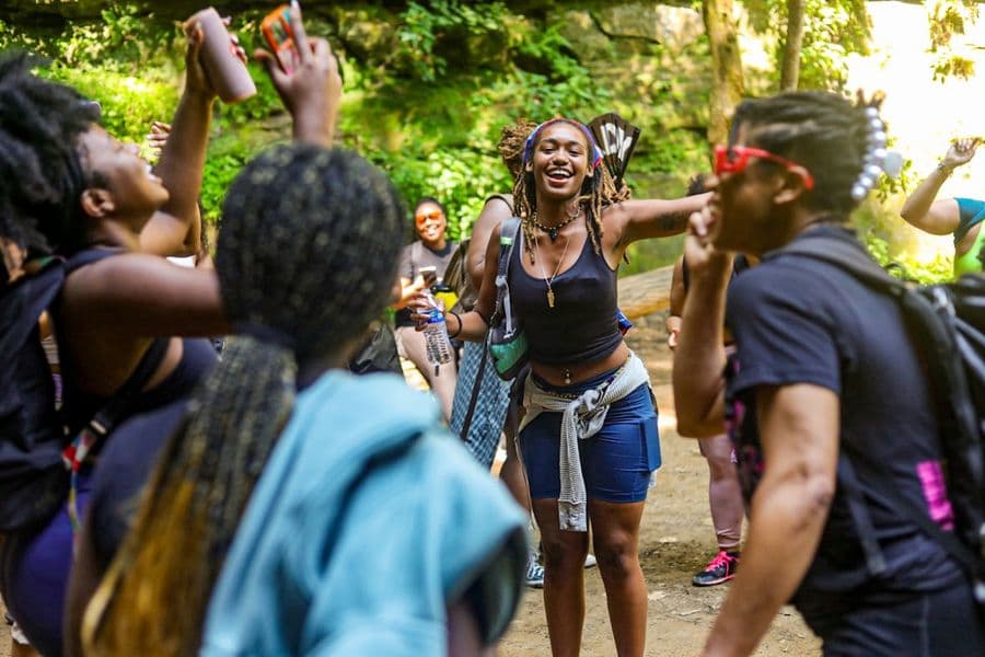 A group of Black women cheering with trees in the background. 