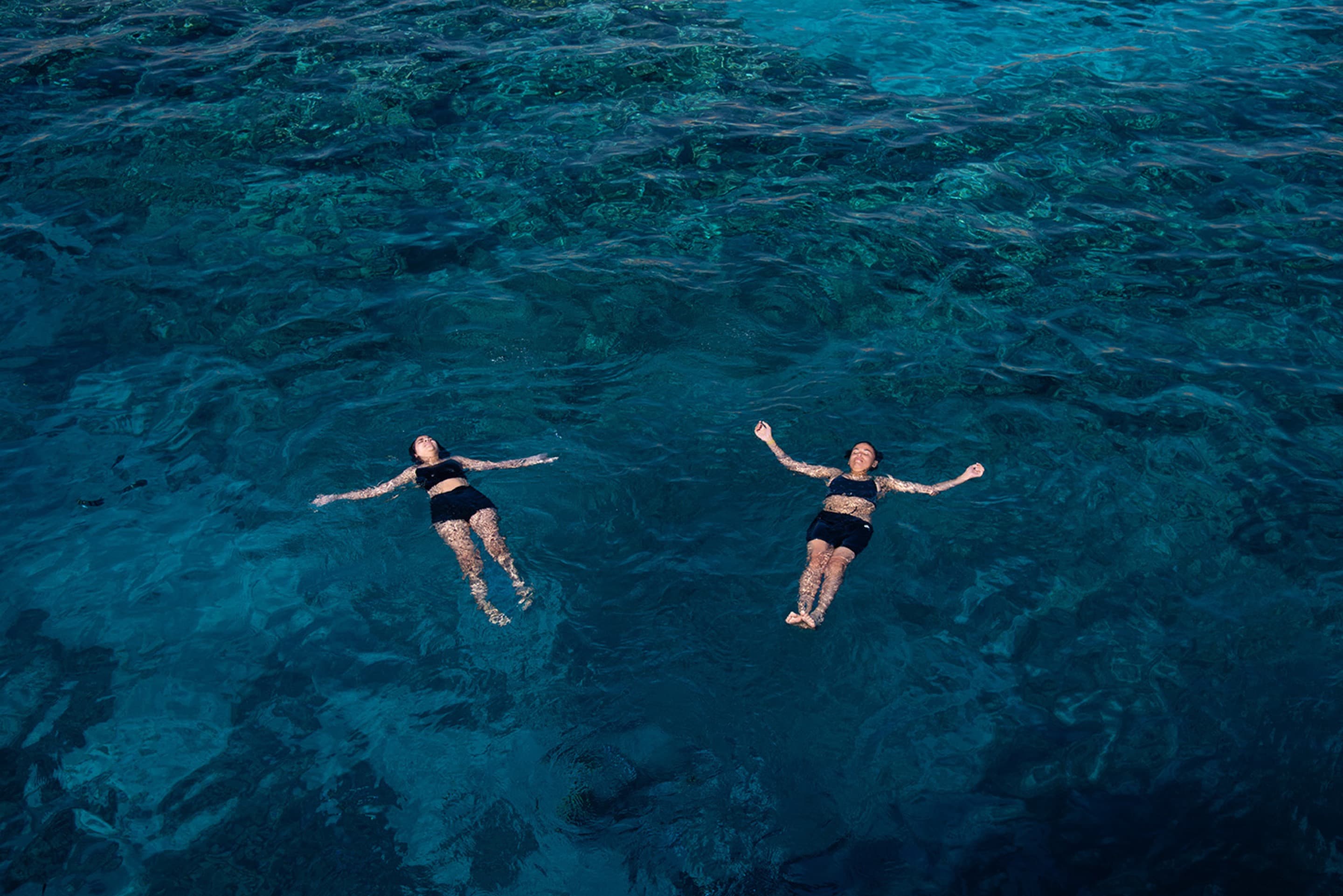 Two women float with their arms out in the ocean. 