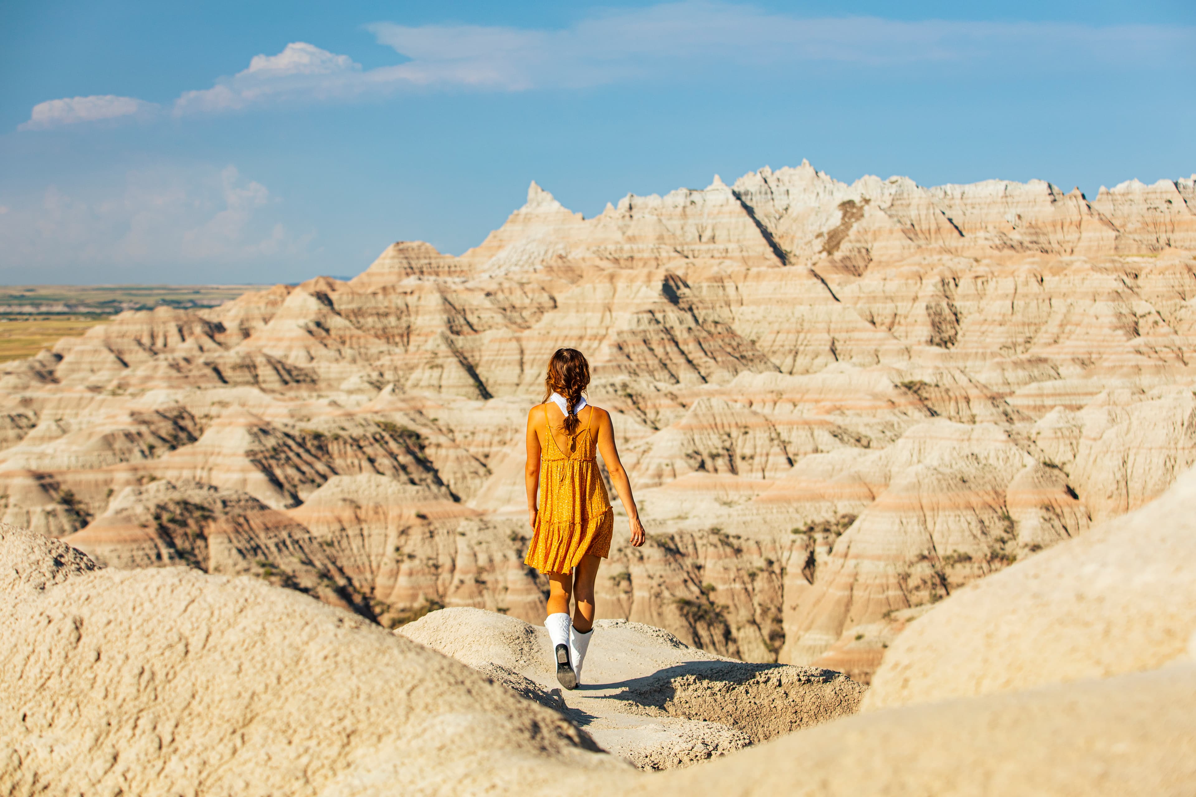 A young woman in a yellow dress walking towards a mountain. 